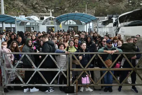 Getty Pictures di una grande folla di persone di una miscela di secoli che trasportavano borse dietro il cancello. Sono rimasto di fronte alla stazione dei traghetti e ci sono grandi autobus accanto a loro